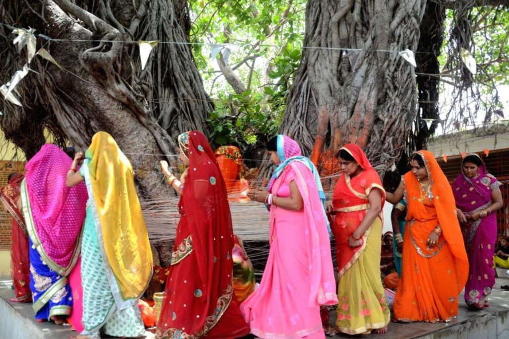 Married women performing Vat Savitri Vrat by worshipping a banyan tree, tying sacred threads, and offering prayers for their husband’s long life.
