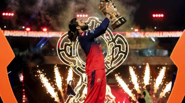 Rajat Patidar, captain of Royal Challers Bengaluru, lifting the IPL 2026 trophy during a grand celebration in a brightly lit cricket stadium.